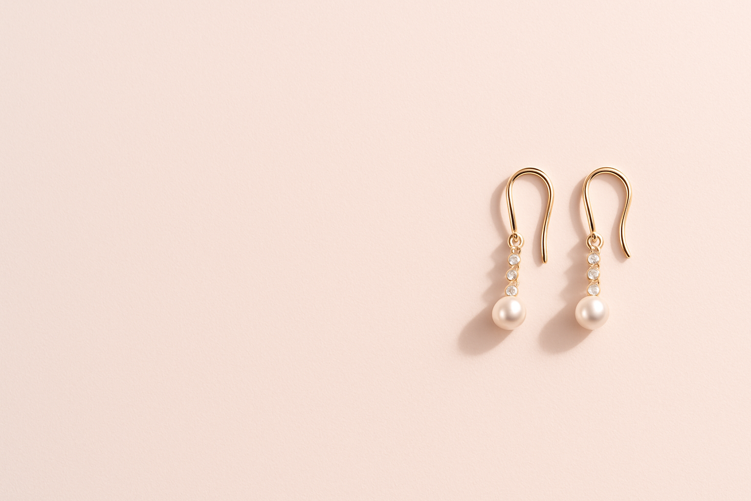 Minimalist flat lay of a pair of elegant gold earrings placed completely at the far right edge of the frame on a solid background with color #fdf0eb, leaving wide empty space on the left. Ultra bright, very clean and refined luxury aesthetic, almost white background with a soft pink hue, soft natural shadows, high resolution, sophisticated jewelry photography.
